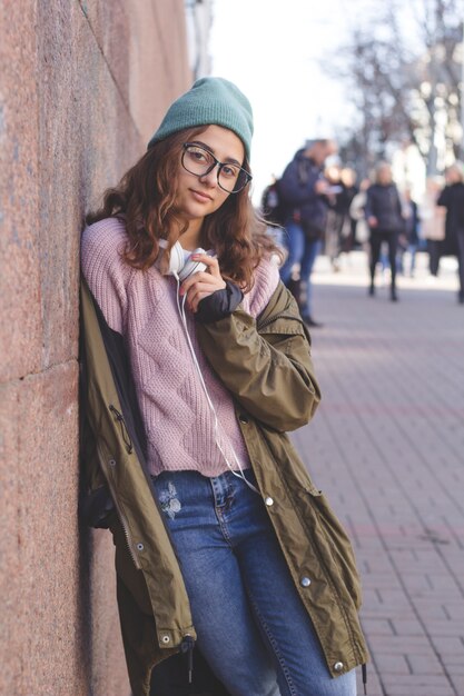 Cute teen girl in a hat and headphones on a city street. Young stylish woman outdoor. 