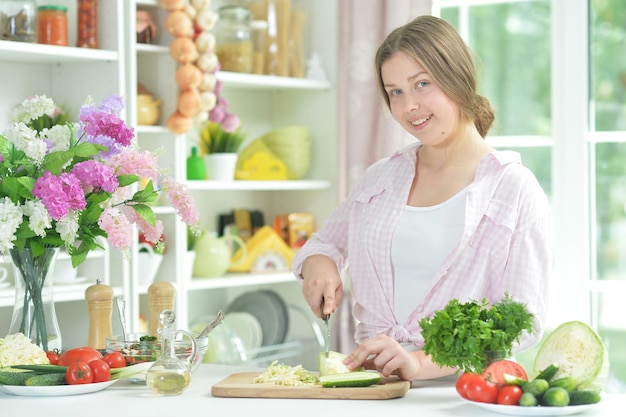 Cute teen girl preparing fresh salad on kitchen table