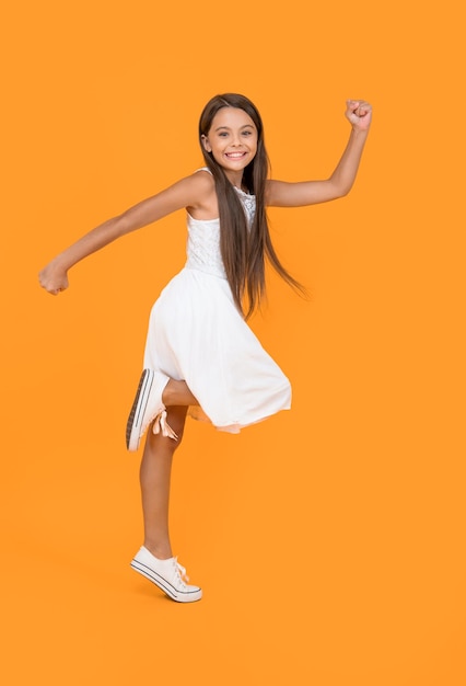 Cute teen girl in white dress running on yellow background