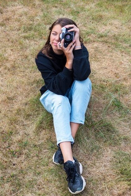 Photo cute teen girl with a camera a girl taking pictures on a retro vintage camera on the grass