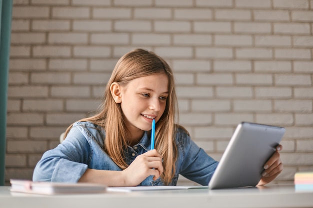 Cute teen schoolgirl does her homework with a tablet at home.