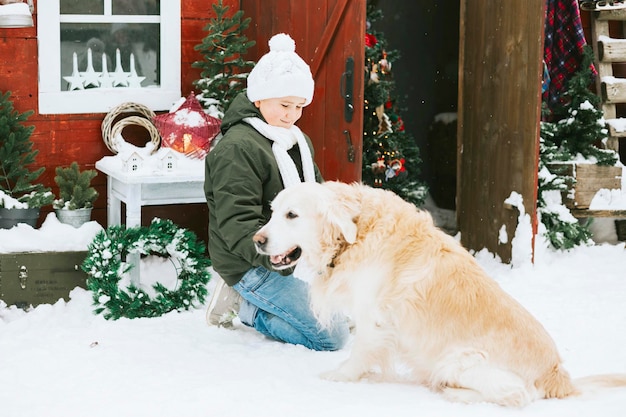 cute teenage boy in knitted sweater and hat having fun with first snow and cute pet dog labrador