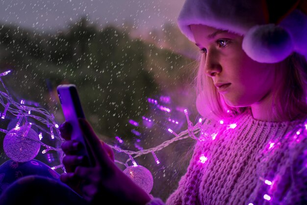 Photo cute teenage girl in santa hat using mobile on snowy day during christmas holidays