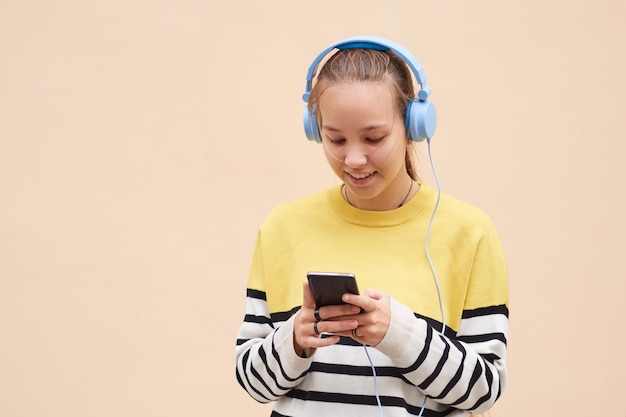 파란색 헤드폰을 사용하여 스웨터를 입은 귀여운 10대 소녀가 컬러 배경에서 음악을 듣고 있습니다.