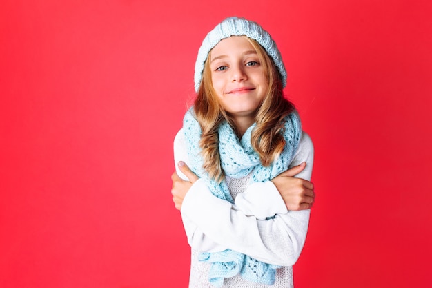 Cute teenage girl in white sweater standing isolated on red wall