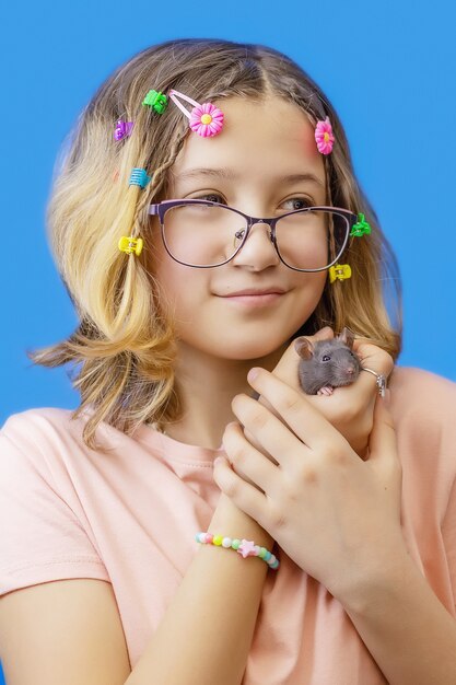 色の背景にペットのネズミを保持しているメガネとかわいい10代の少女