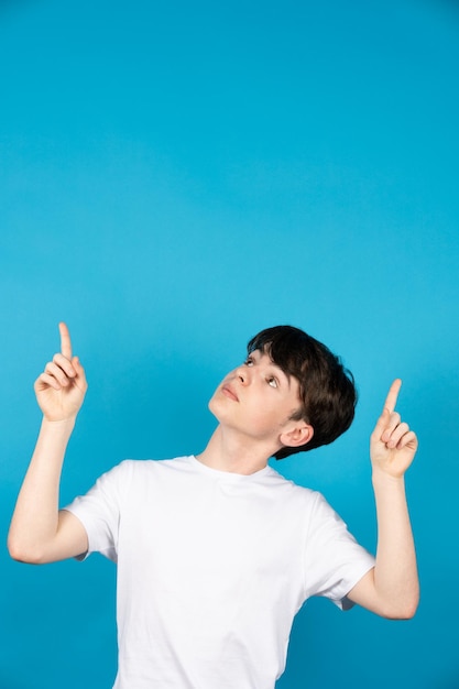 Cute teenager boy pointing up to blue copy space