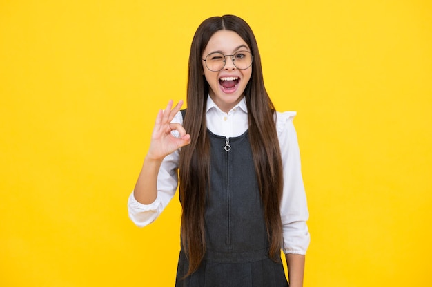 Cute teenager child girl making Ok gesture on yellow background Excited face cheerful emotions