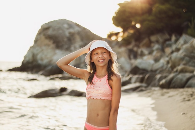 かわいいティーンエイジャーの女の子が、夏の日の終わりに海岸に沿って歩いています。