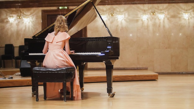 Cute teenager girl plays piano in the concert hall at scene telephoto