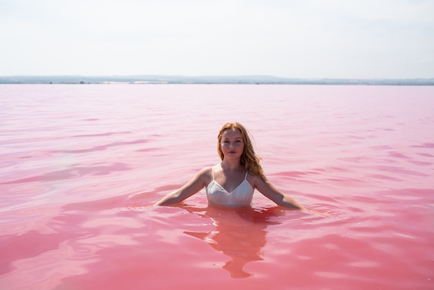 Foto ragazza sveglia dell'adolescente che porta vestito bianco nell'acqua di un lago rosa stupefacente