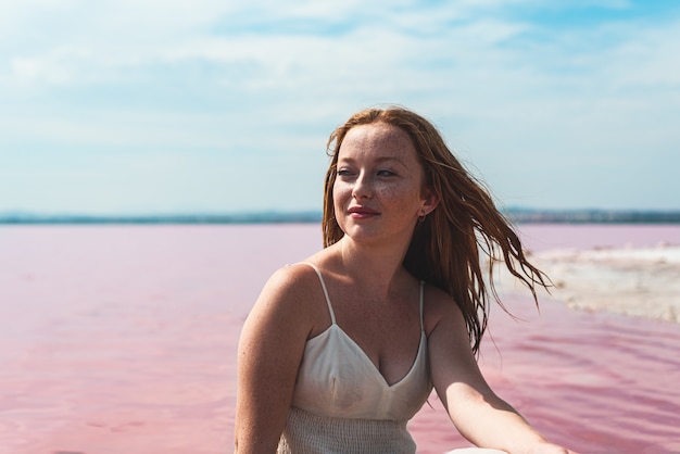 Vestito bianco da portare dalla donna sveglia dell'adolescente che si siede su un lago rosa stupefacente