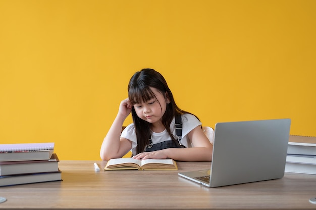 A cute and thoughtful young Asian girl focusing on reading a book at her study table