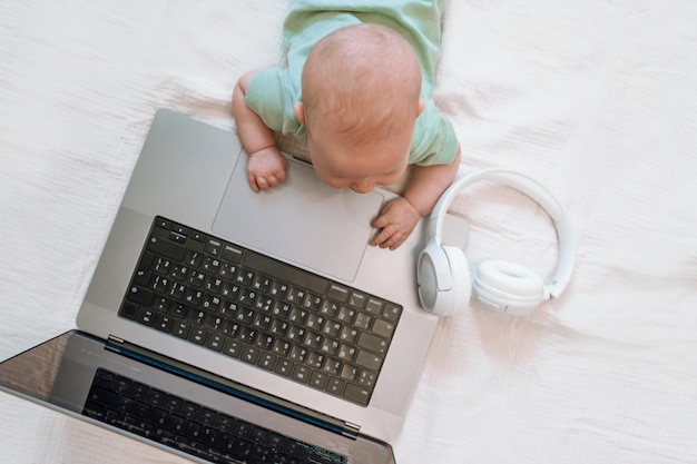 A cute three-month-old baby is lying in front of a laptop. A funny concept of a business kid program