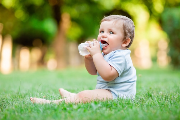 Cute toddler boy in blue bodysuit sitting on the grass