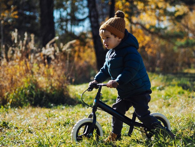 Foto un bambino carino in abiti casuali che va in bicicletta in autunno nella foresta.