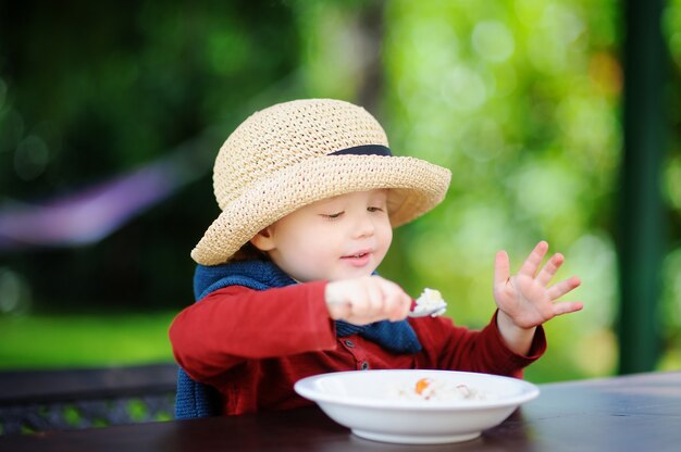 야외에서 쌀 시리얼을 먹는 귀여운 유아 소년. 어린 아이들을위한 건강에 좋은 음식