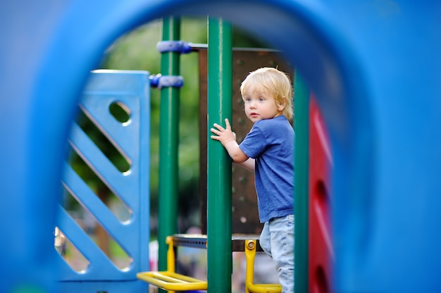 Cute toddler boy having fun on outdoors playground. Active game for little kids