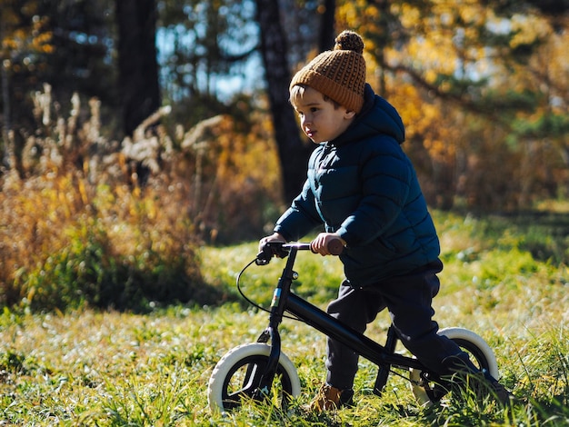 Фото Милый мальчик в обычной одежде едет на велосипеде в осеннем лесу.