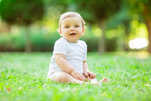 Милый малыш мальчик в белом боди сидит на траве