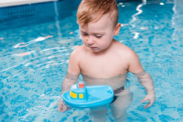 Cute toddler boy looking at toy ship in swimming pool