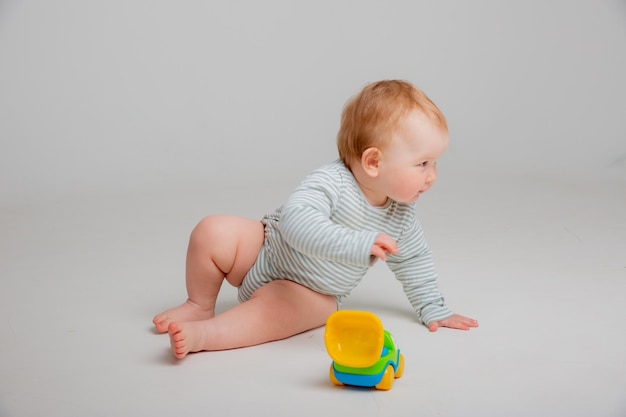 白いボディスーツを着たかわいい幼児の男の子は、テのための白い背景のスペースに座って車のおもちゃで遊んでいます