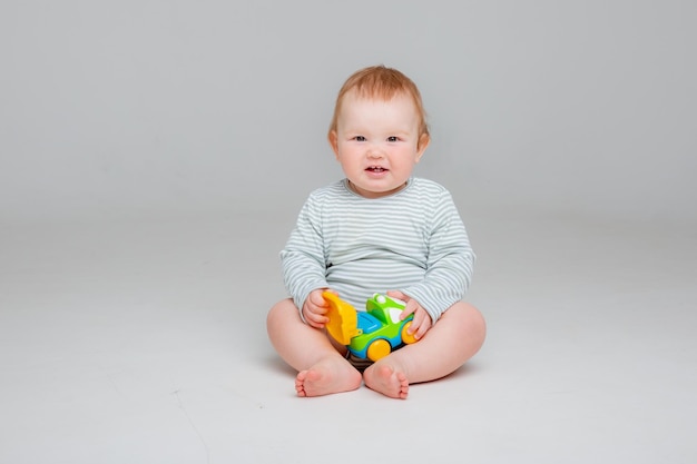 白いボディスーツを着たかわいい幼児の男の子は、テのための白い背景のスペースに座って車のおもちゃで遊んでいます