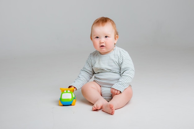 Cute toddler boy old in white bodysuit plays with car toy sitting on a white background space for te