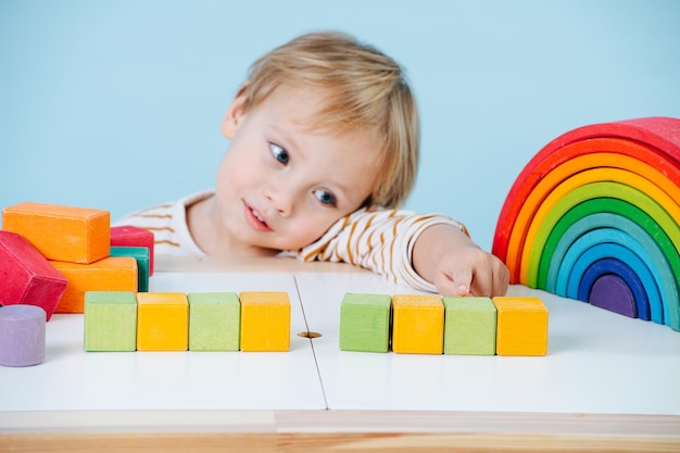 Foto ragazzo sveglio del bambino che gioca con i cubi colorati del giocattolo su un tavolo sopra il blu