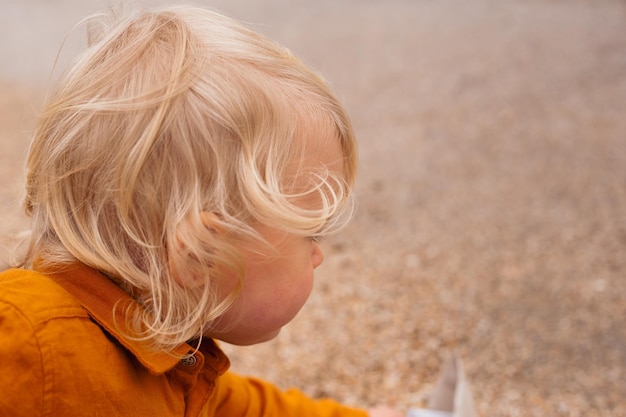 Cute toddler boy playing with paper boat on the beach in autumn time