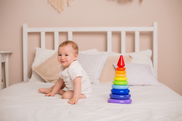 Cute toddler boy smiles sitting on bed with multi-colored pyramid