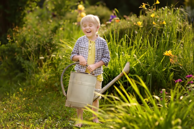 Cute toddler boy watering plants in the garden at summer sunny day.