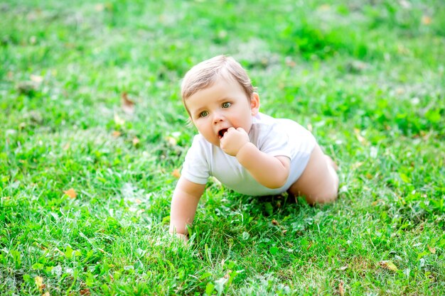 草の上に座っている白いボディースーツでかわいい幼児男の子