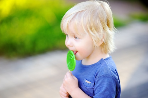 Ragazzo carino bambino con grande lecca-lecca verde. bambino che mangia dolce candy bar. dolci per bambini piccoli. divertimento estivo all'aperto