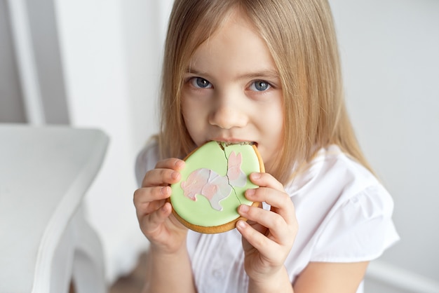 白いシャツを着たかわいい幼児の女の子がクッキーを食べています。