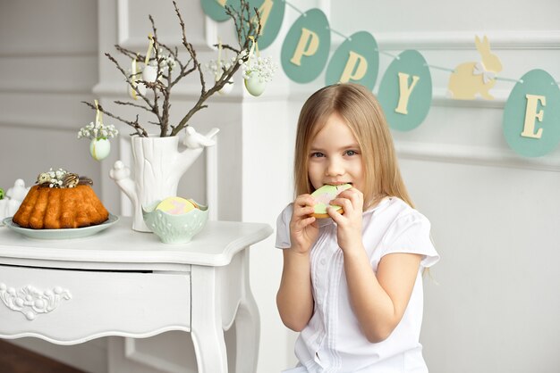 白いシャツを着たかわいい幼児の女の子がクッキーを食べています。