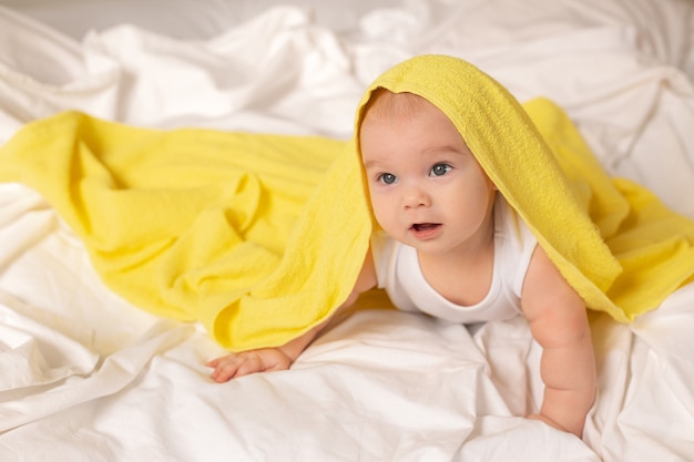 Cute toddler lies in bed with yellow towel after bathing