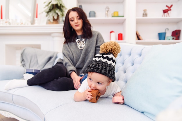 Cute toddler lies on the blue couch and happy young mommy kneading his legs and makes him happy.