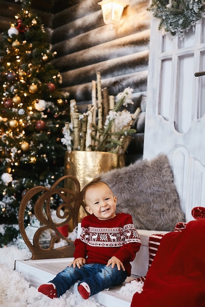 Cute toddler in ugly sweater posing on the stairs of the decorated for Christmas house.