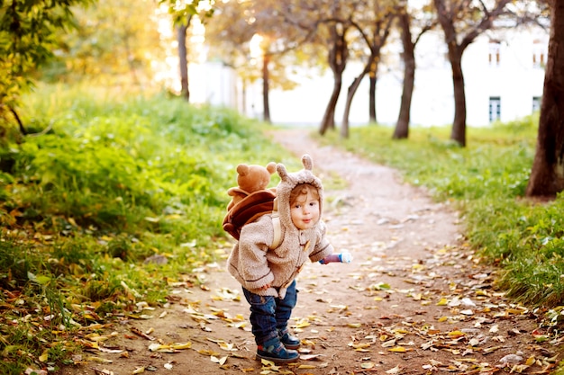 Bambino sveglio in vestiti caldi divertendosi nel parco nella caduta dorata