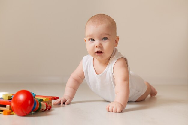 白いボディー スーツを着たかわいい幼児が、家の木の床におもちゃを持って横たわっている