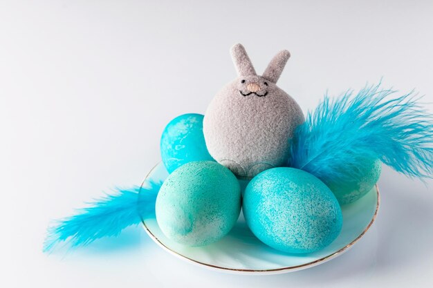 Cute toy easter bunny and blue painted eggs with feathers on  white background Place for your text