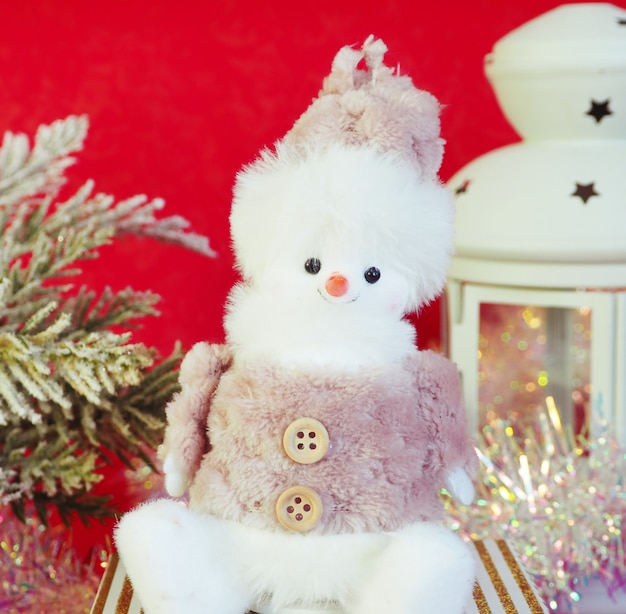 Cute toy snowman, spruce branches, tinsel and a candlestick on a red background.