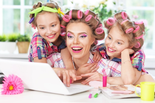 Cute  tweenie girls and mother  in hair curlers  with laptop at home