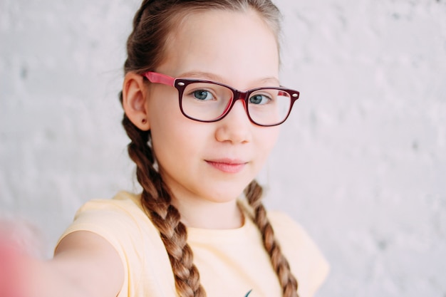 Cute tweens girl in yellow t-shirt with funny pigtails taking selfie on frontal camera 