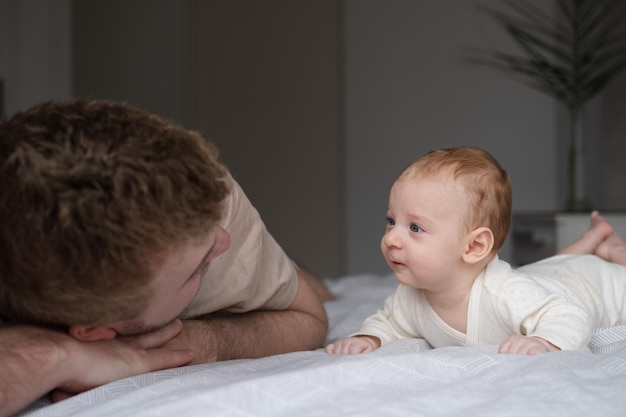 Cute two or three months baby boy looking at his parent or adult lying on belly on bedcopy space