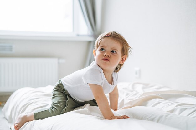 自宅のベッドの上に座って家の服でかわいい動揺赤ちゃん女の子怒っている子