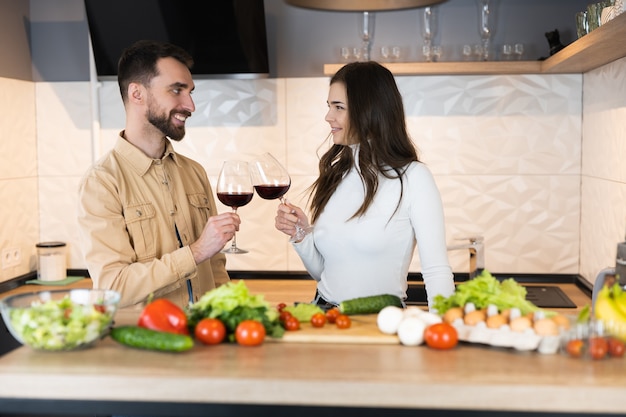 Cute vegetarian couple are cooking and drinking red wine together on a date in domestic kitchen.