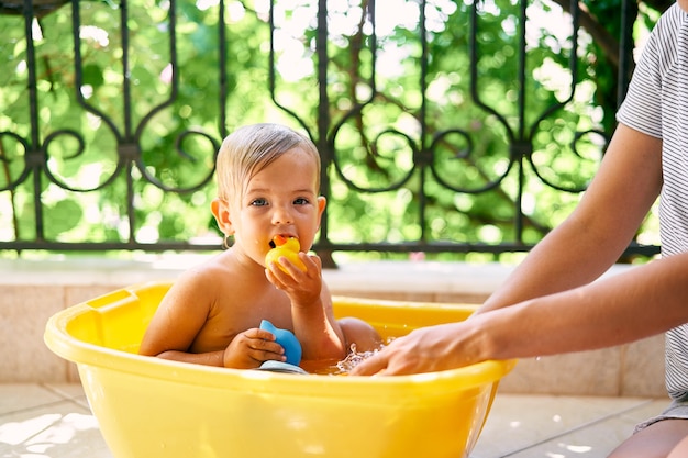 Un bel bambino bagnato si siede in una bacinella e rosicchia un giocattolo Foto Premium