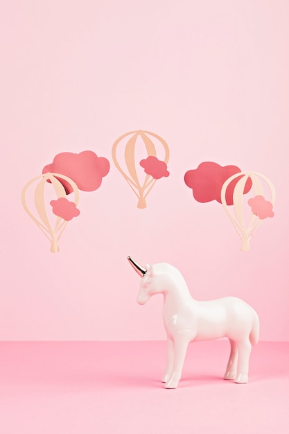 Cute white unicorn over the pink pastel background with clouds and ballons